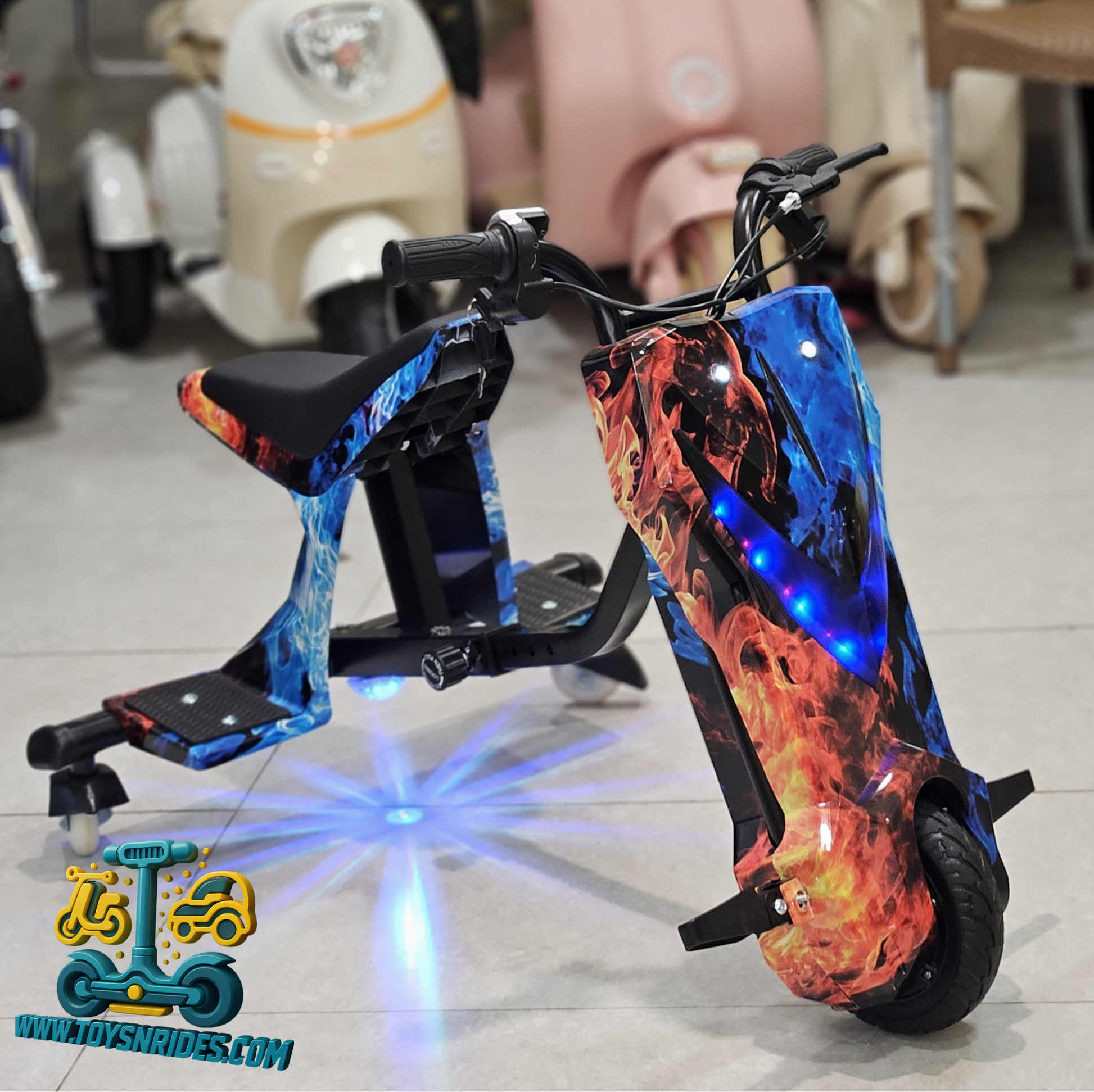 3 wheel E-scooter with flame-patterned design on a tiled floor, brand 'TOYSNRIDES' visible.