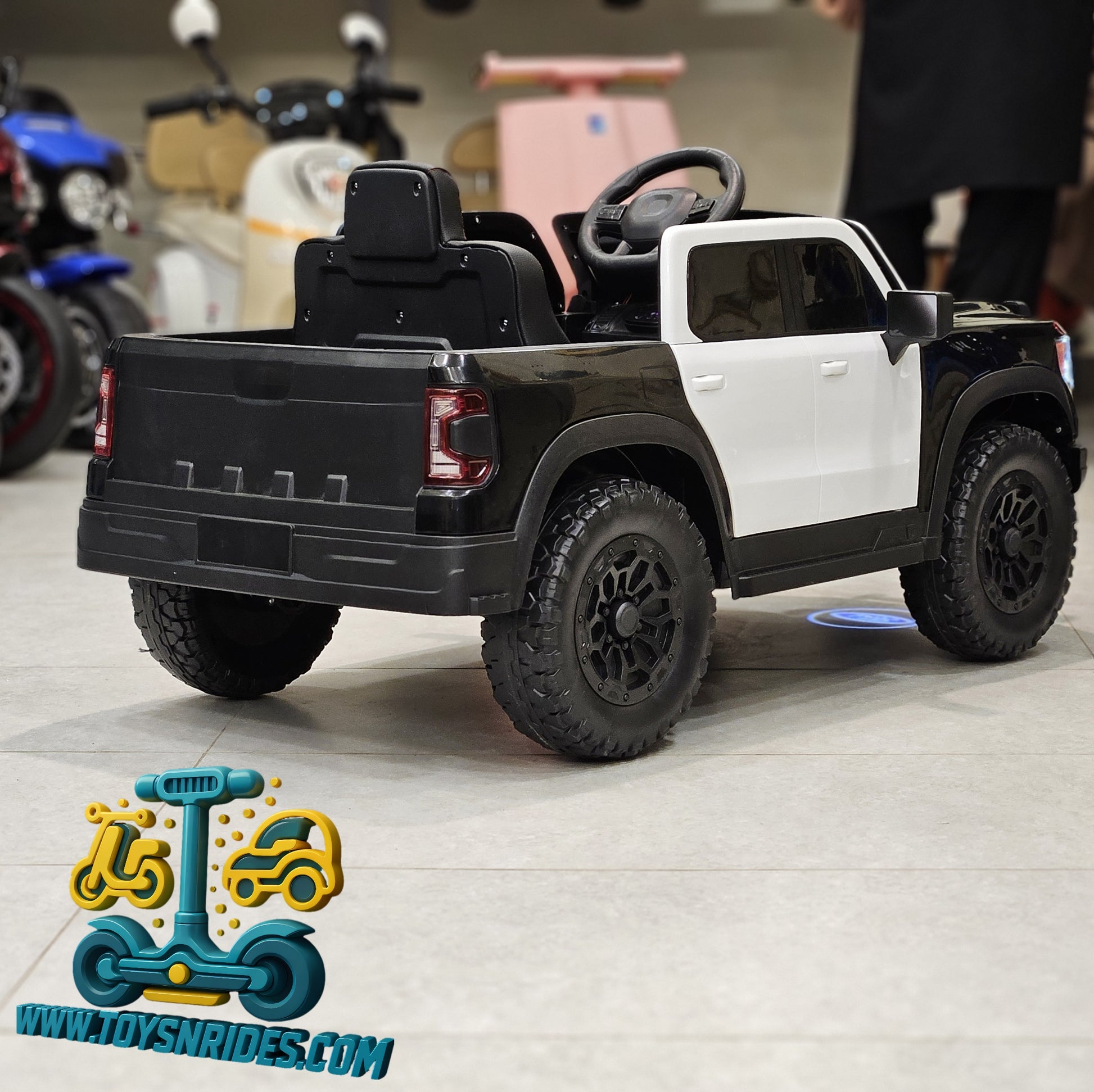 Black and white toy truck on a light wooden floor with 'www.toysnrides.com' logo.