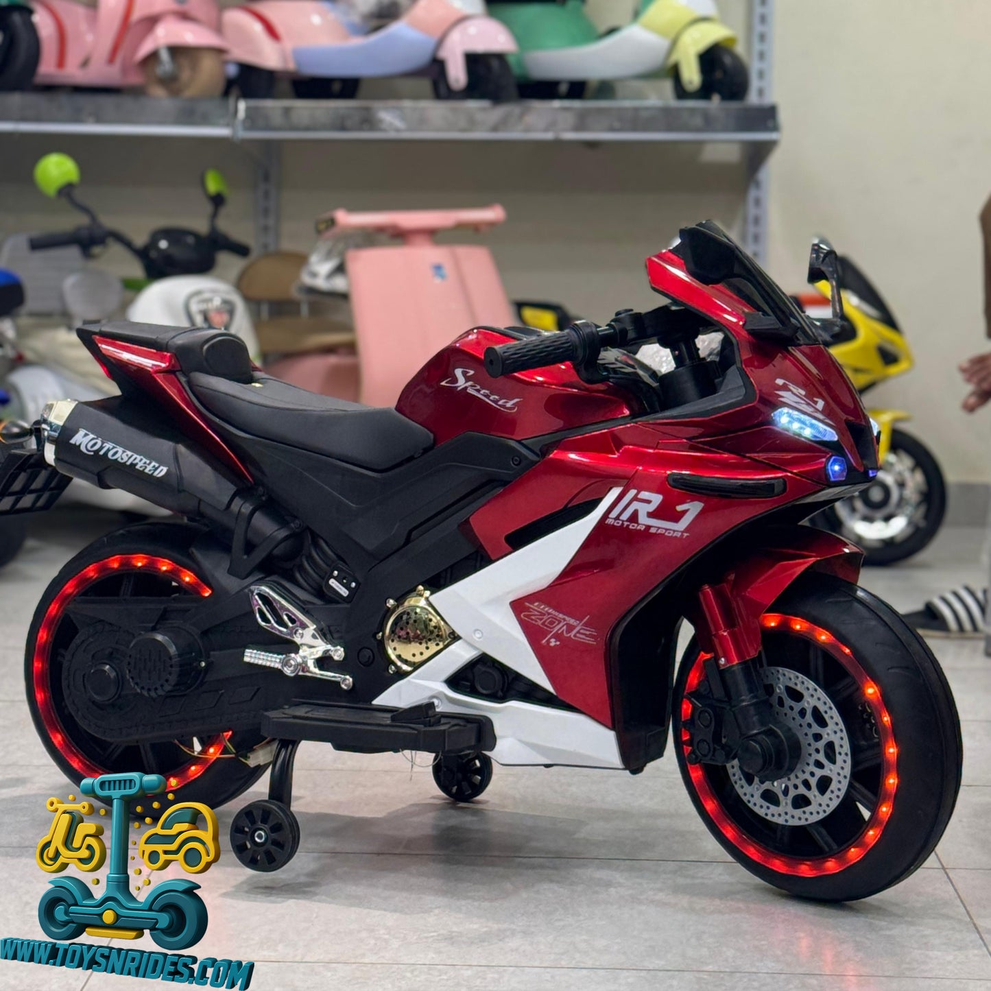 Red and black toy motorcycle with LED lights on a shelf with other toys.