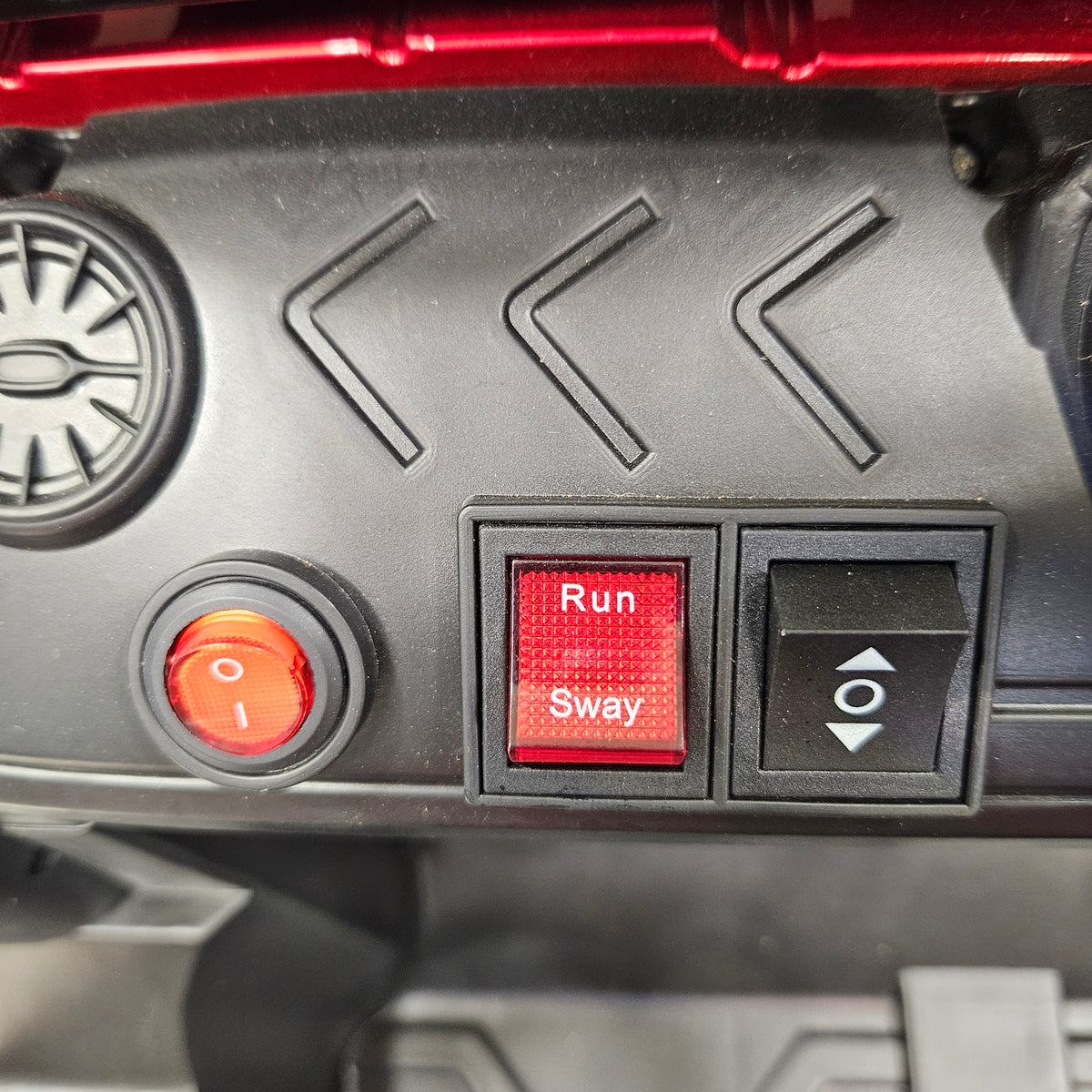 Close-up of a black vehicle or machinery control panel with a red 'Run' and 'Sway' button, a red power switch, and a black toggle switch.